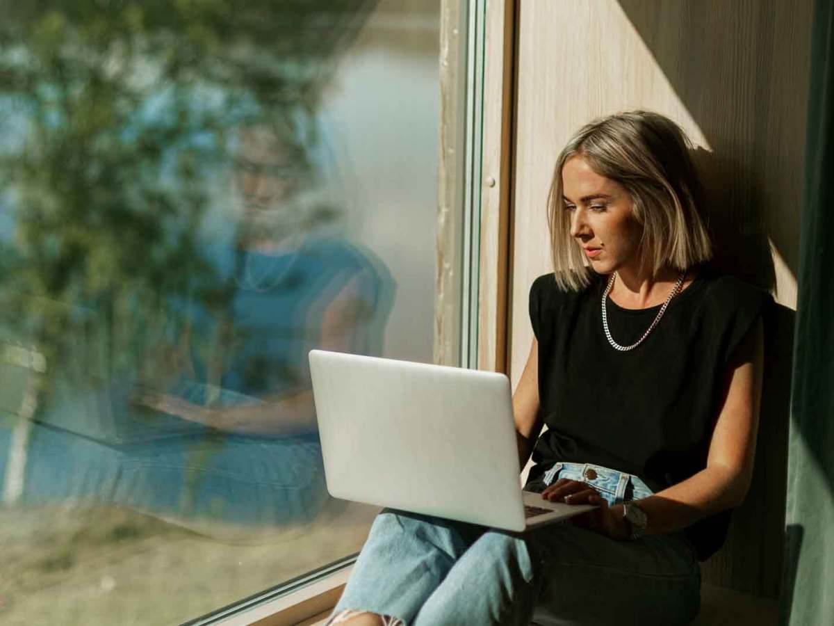 Frau sitzt am Fenster vor ihrem Laptop.